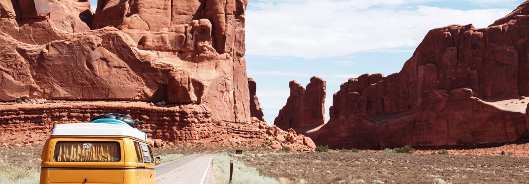 Yellow Bus Driving on Road Through Rocky Canyon