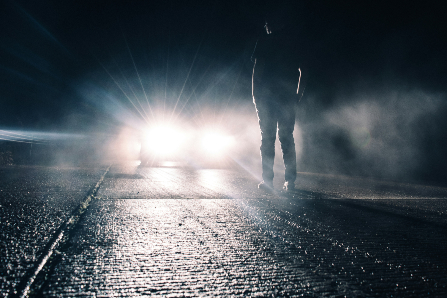 Man standing in front of car with headlights on in the dark