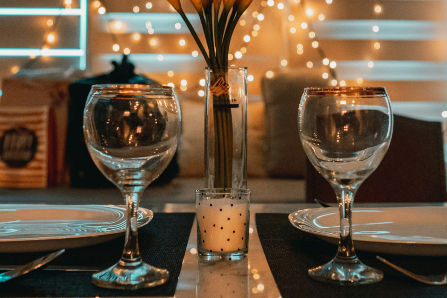 Two wine glasses set at table with candle, flowers, and twinkle lights
