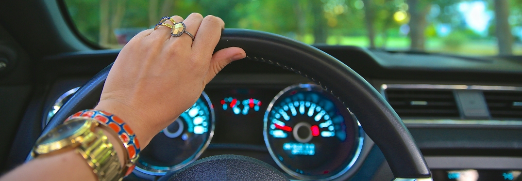 Woman wearing rings and bracelets with hand on steering wheel of car