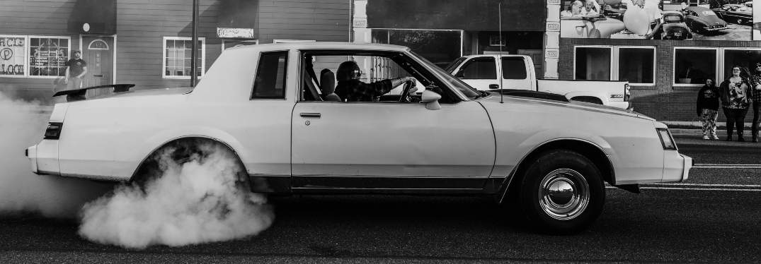 Black and white photo of old car with smoking tires